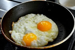 Two fried eggs sizzling in a black pan