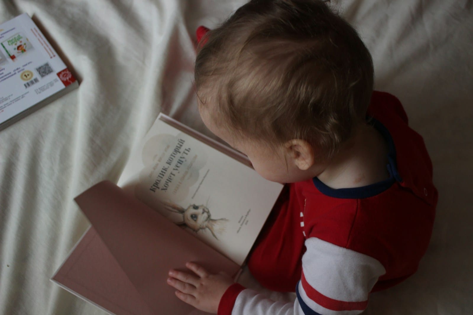 Photo by Iana Dmytrenko baby sitting on bed while reading on book